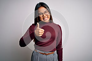 Beautiful asian business woman wearing casual sweater and glasses over white background doing happy thumbs up gesture with hand