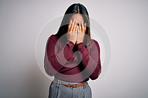 Beautiful asian business woman wearing casual sweater and glasses over white background with sad expression covering face with