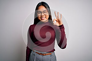 Beautiful asian business woman wearing casual sweater and glasses over white background smiling positive doing ok sign with hand