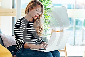 Beautiful asian business woman working and typing with laptop while sitting on couch in coworking place