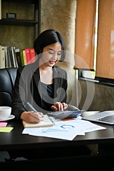 A beautiful Asian businesswoman calculates sales using a calculator and laptop