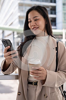 A beautiful Asian businesswoman is responding to messages on her phone while she is in the city