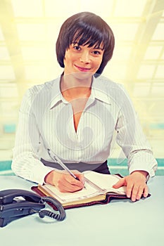 beautiful asian businesswoman sitting at the table writing looking at camera and smiling instagram stile