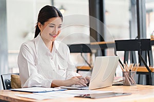 Beautiful asian businesswoman smiling while working with laptop computer at a Modern Co working Space. Remote work