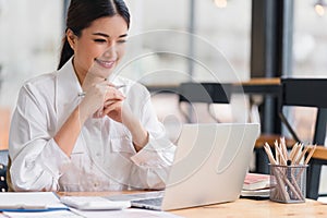 Beautiful asian businesswoman smiling while working with laptop computer at a Modern Co working Space. Remote work