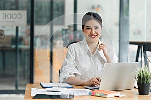 Beautiful asian businesswoman smiling while working with laptop computer at a Modern Co working Space. Remote work