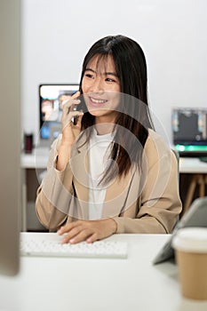 Beautiful Asian businesswoman is talking on the phone with her client at her desk in the office