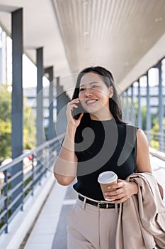 A beautiful Asian businesswoman is talking on the phone while walking on a skywalk in the city