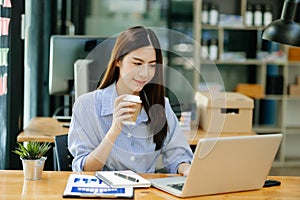 beautiful Asian businesswoman typing laptop computer and digital tablet while holding coffee at office