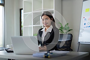 Beautiful asian businesswoman woman using calculator and laptop for doing finance on an office desk, tax, report