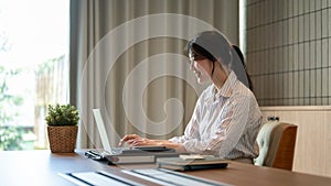 A beautiful Asian businesswoman working on her laptop at a meeting table in a meeting room alone