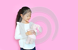 Beautiful asian child girl holding pink fluffy rabbit doll isolated on pink background with copy space. Happy Kid on Easter