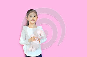 Beautiful asian child girl holding pink fluffy rabbit doll isolated on pink background with copy space. Happy Kid on Easter