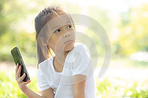 Beautiful asian child smiling using smart mobile phone in the garden, kid have passion playing game digital on smartphone