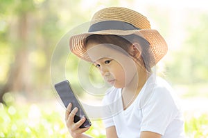Beautiful asian child smiling using smart mobile phone in the garden, kid have passion playing game digital on smartphone
