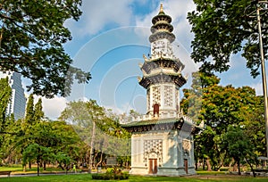 Beautiful asian clock tower among fresh green tree in park on blue sky background