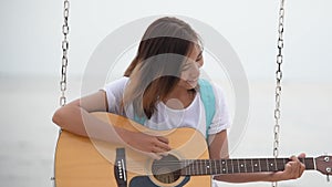 Beautiful asian cute girl playing acoustic guitar on the beach. Woman wear casuak white t-shirt sitting on tropical beach summer i