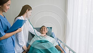 Beautiful Asian doctor listens to heart patient in hospital bed.