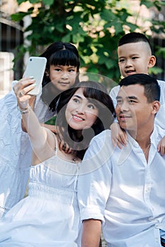 Beautiful asian family in white clothes taking selfie in a park, having picninc