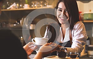 Beautiful Asian female barista serving hot coffee to customer at counter bar background. Smiling woman and occupation