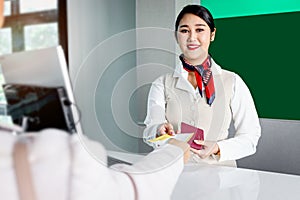 Beautiful Asian female passenger service agent receives passport boarding pass from traveler, checking information at check in