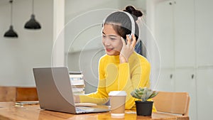 A beautiful Asian female student is listening to music while working on her laptop in a library