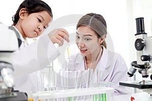 Beautiful Asian female teacher in lab coats teaching schoolgirl child to do science experiments. Happy young scientist kid girl