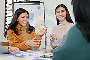 Beautiful Asian female UI designer discussing and presenting her new prototype with her team