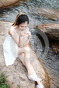 Beautiful asian female in white dress is hand holding grass flower on the rock and stream in tropical forest