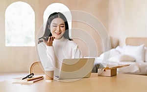 Beautiful Asian Freelancer woman holding phone speak activate virtual digital voice assistant or loudspeaker talking on smartphone