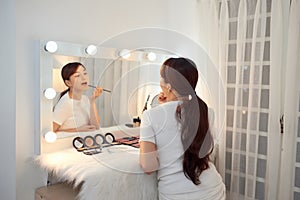 Beautiful Asian girl applying lipstick watching in mirror at makeup table