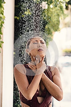 Beautiful asian girl in a bikini taking a shower in a bungalow yard.