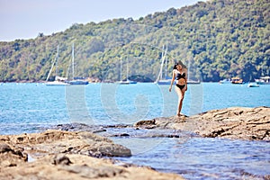 Beautiful asian girl in a black bikini posing on a beach with rocks