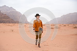 Beautiful asian girl in boots and a cowboy hat walks through the desert