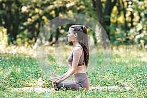 Beautiful Asian girl doing yoga in the forest meditating sitting in lotus pose side view