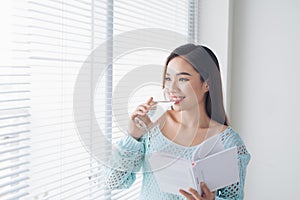 Beautiful asian girl drinking water and reading book near window