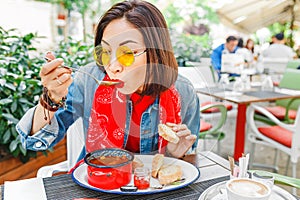 Beautiful asian girl eating hungarian goulash soup from a decorative red casserole in outdoor restaurant