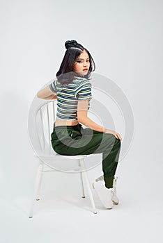 Beautiful asian girl in fashionable in croptop sitting on stool and looking at camera