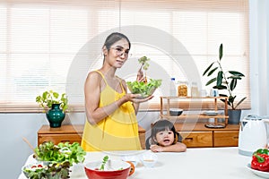 beautiful Asian girl and her lovely daughter are cooking in kitchen, The daughter sitting was eating sausage on her lap, both her