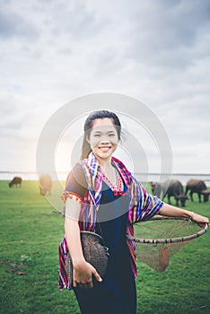 Beautiful Asian girl holding fish trap and basket, prepare to catch fish walking in field near lake