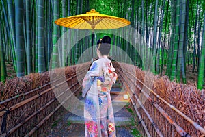 Beautiful Asian girl in kimono holding an umbrella visits a bamboo forest in Kyoto, Japan