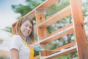 Beautiful Asian girl paiting wooden shelf by roller