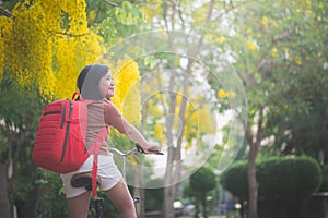 Beautiful Asian girl with red backpack riding bicycle in the park