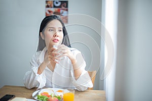 Beautiful asian girl sitting and holding a glass of milk with an absent minded expression while looking to the copy space