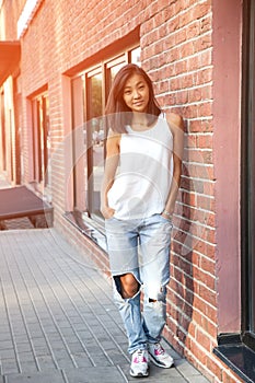 Beautiful Asian girl in sports style stands near the city brick wall