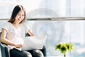 Beautiful Asian girl using laptop computer. College student or freelance worker in modern office. Education or business concept photo