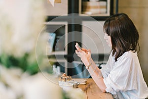 Beautiful Asian girl using smartphone at cafe with chocolate toast and ice cream. Coffee shop dessert and modern casual lifestyle