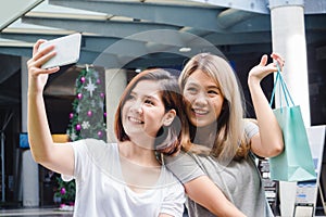 Beautiful asian girls holding shopping bags, using a smart phone selfie and smiling while standing outdoors.