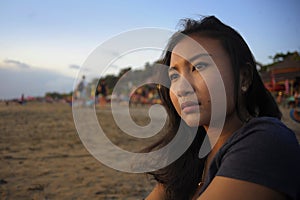 Beautiful Asian lonely woman looking to infinity lost in her thoughts sad and thoughtful sitting on sand beach