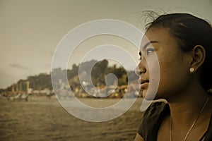 Beautiful Asian lonely woman looking to infinity lost in her thoughts sad and thoughtful sitting on sand beach